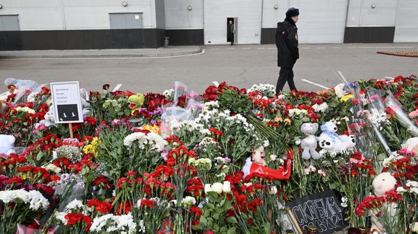 Сотрудник полиции у стихийного мемориала у здания концертного зала Крокус Сити Холл