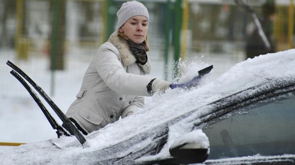 Женщина чистит машину от снега